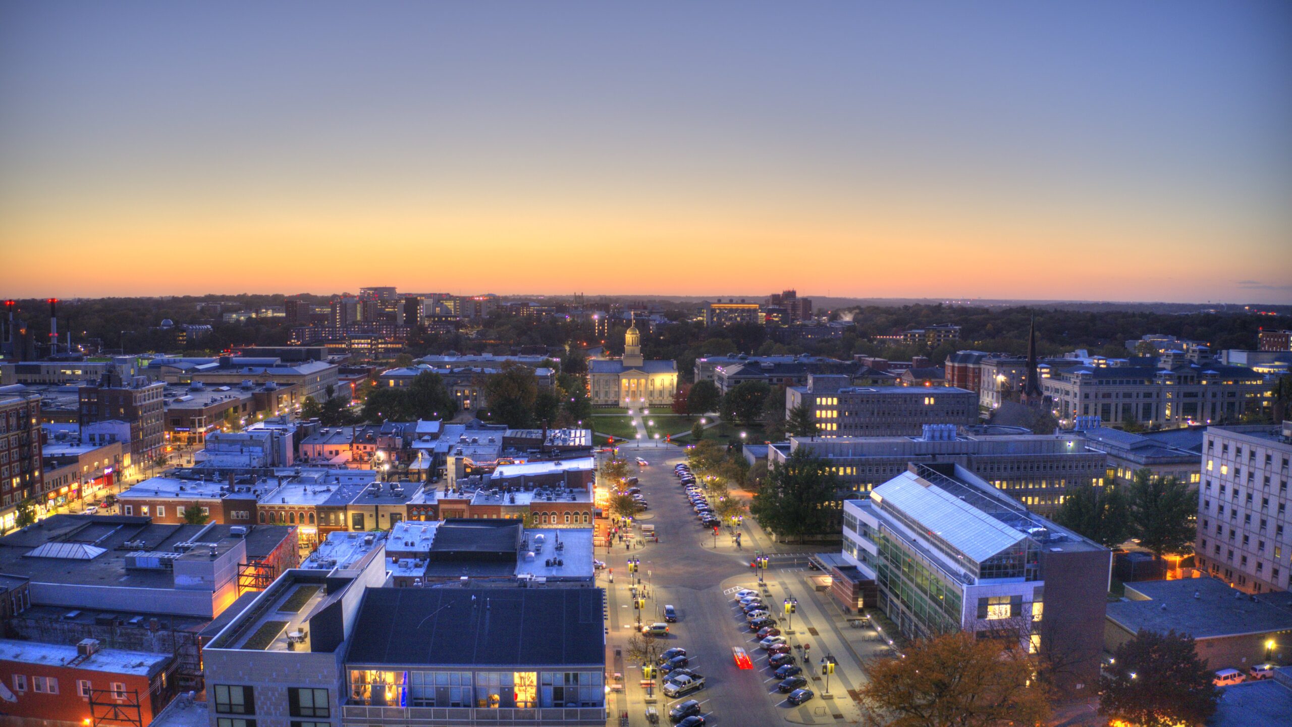 A picture of downtown Iowa City at dusk with the sunset in the background and the road leading up to the Old Capitol Building